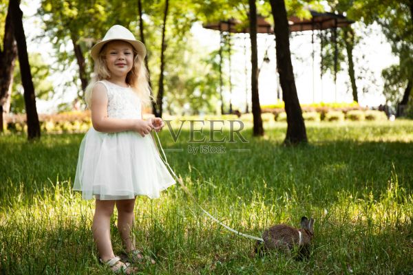 可爱的小女孩遛着宠物兔子，照顾着和动物生活在一起。童年快乐，热爱大自然照片摄影图片