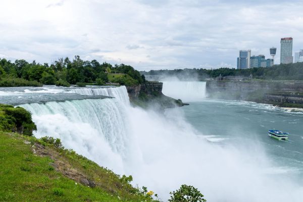 Niagara Falls with misty waters and the Maid of the Mist below, with city buildings in the background.