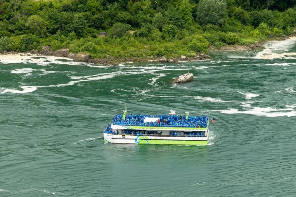 The Maid of the Mist filled with people in blue ponchos floating near lush greenery on a river.