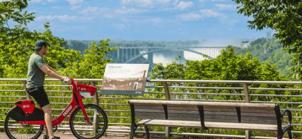 A person riding a red bike by an overlook at Niagara Falls State Park on a sunny day.