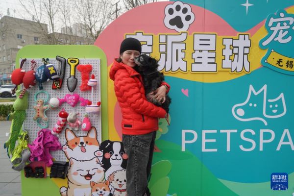 3月15日，在无锡市运河汇街区，一位女士抱着宠物狗在活动展板前打卡。 新华社发（刘臻睿摄）