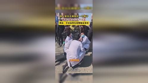 四个白大褂按住一个男孩，路人要求白大褂放开男孩